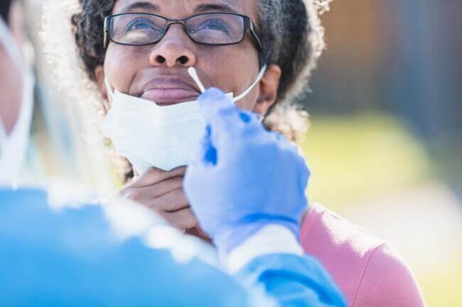 Older African American Woman with mask lowered receiving a nasal swab for COVID test